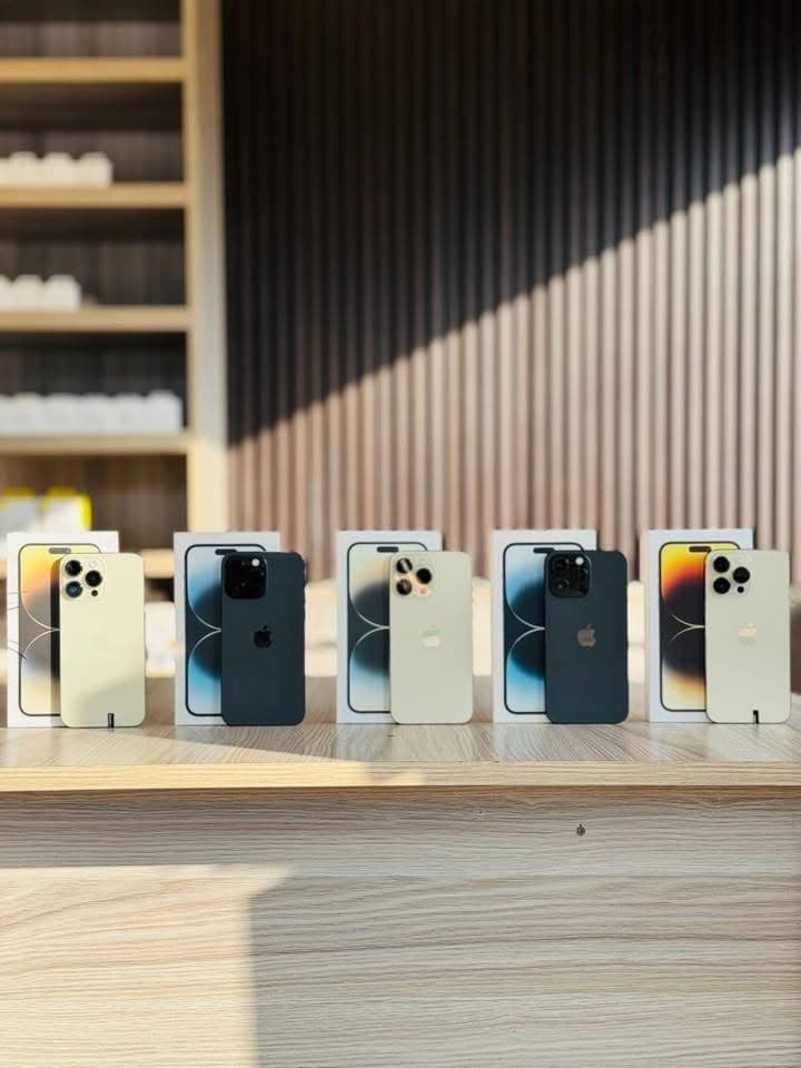 Rear view of five iPhone models showing various color finishes, Apple logo, and camera setups on showroom wooden counter